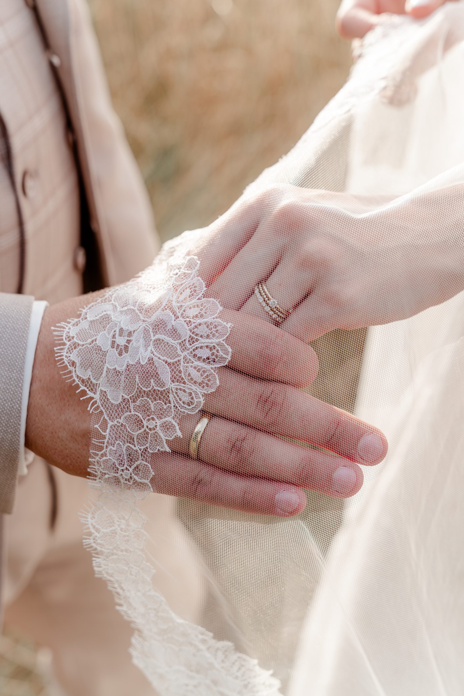 Nahaufnahme: Die Hand der Braut mit Spitzenärmel liegt auf der Hand des Bräutigams, beide tragen ihre Ringe
