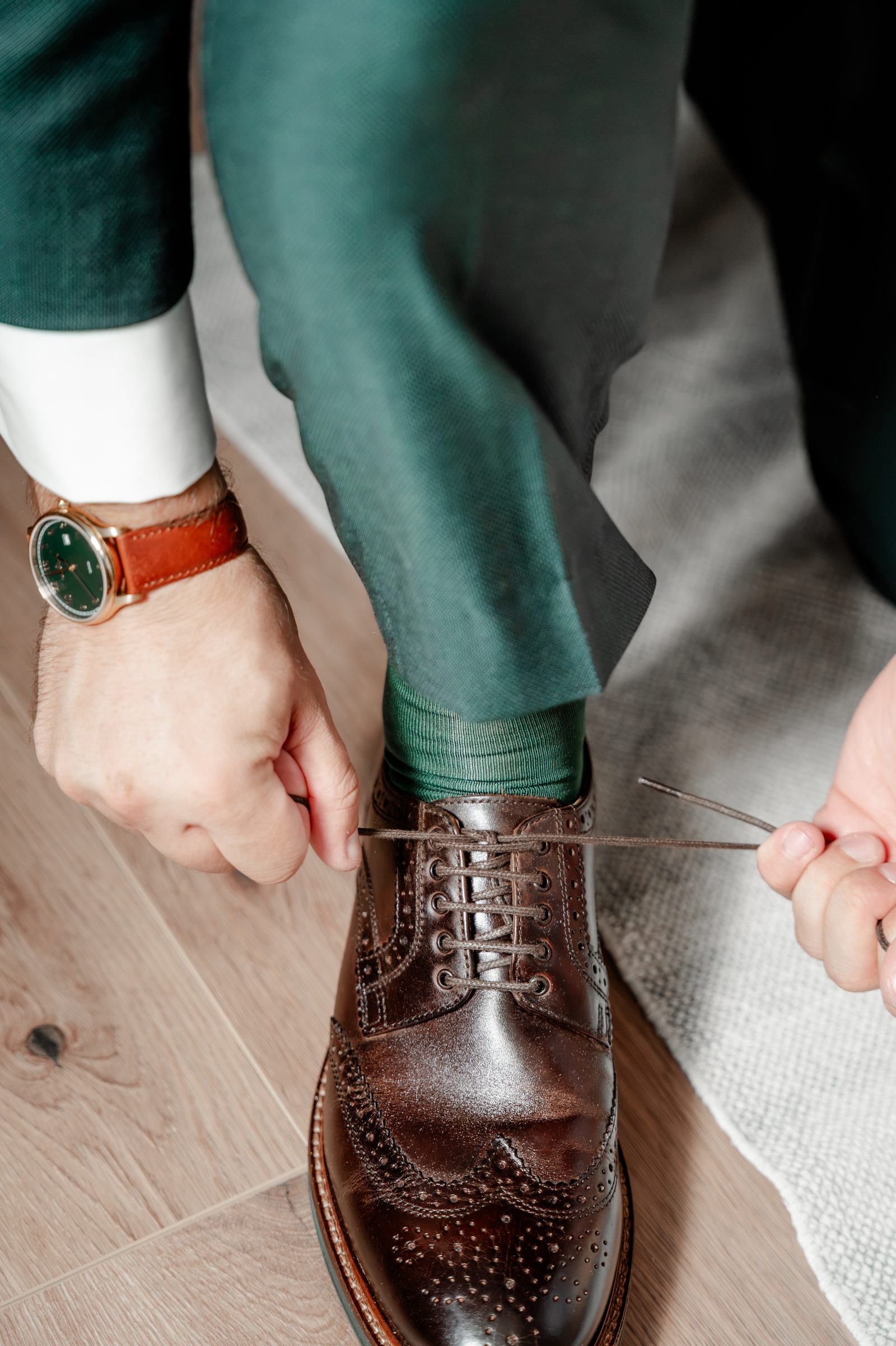 Nahaufnahme: Der Bräutigam schnürt seine braunen Budapester, am Handgelenk eine Uhr mit Lederarmband