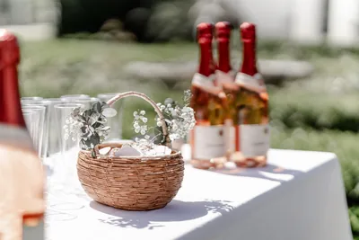 Gedeckter Stehtisch im Garten mit Sektgläsern, einem Weidenkörbchen mit Schleierkraut und Eukalyptus und mehreren Flaschen Sekt